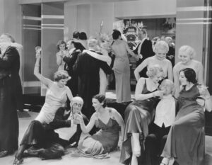 Vintage black-and-white party scene with young women in satin gowns drinking and flirting with older men at a crowded dance